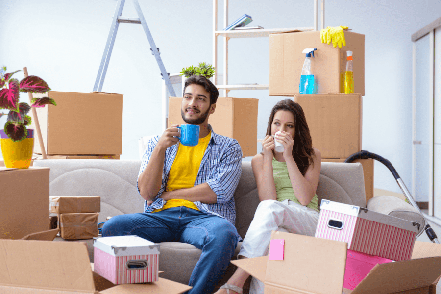 A young couple couple are sitting among  unopened moving boxes and drinking coffee.